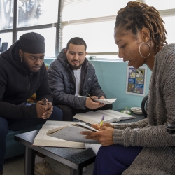 A woman helping two men with schoolwork